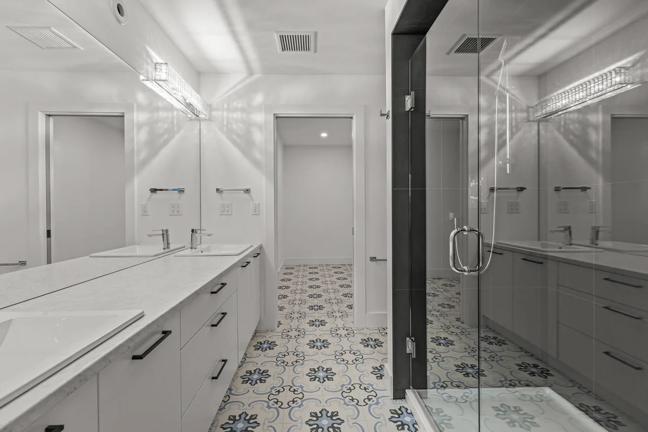 An ensuite with a double vanity, patterned tile floor and a glass walk-in shower