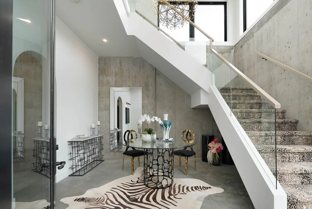 A foyer with a glass and steel staircase, board-formed concrete walls and a round glass table