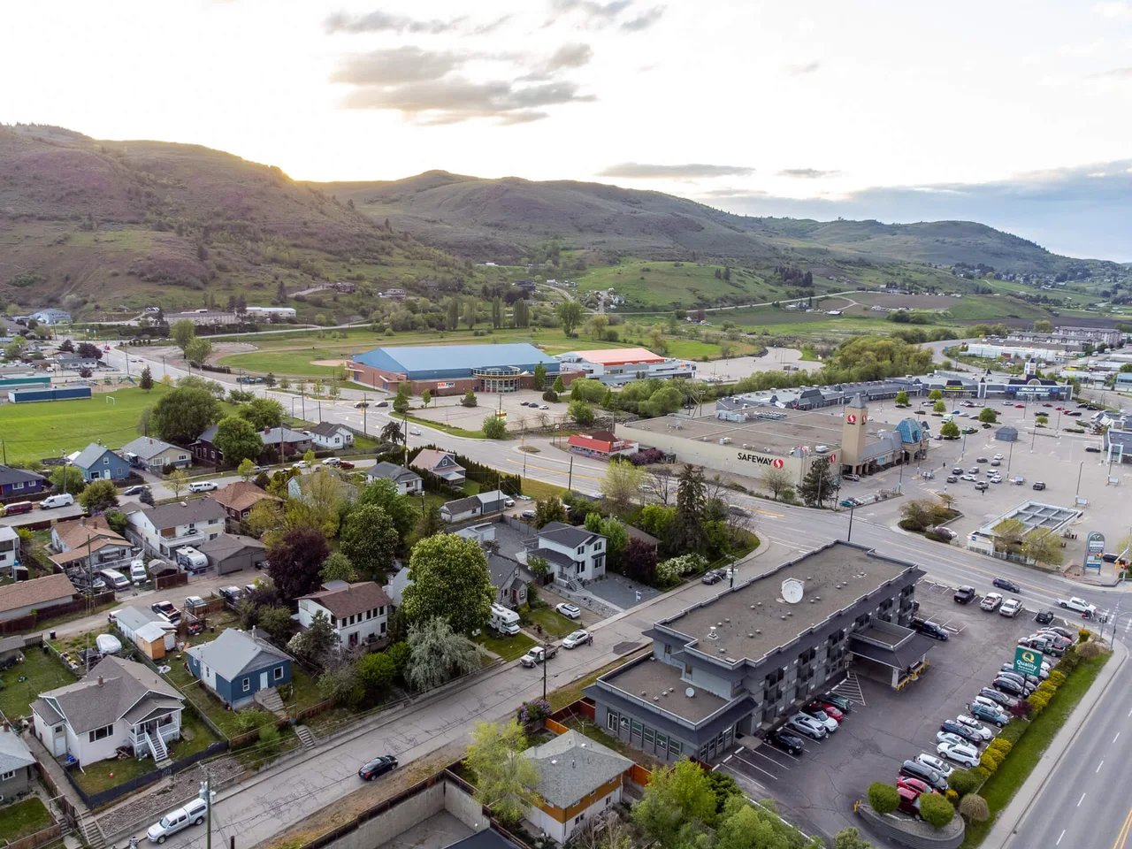 An aerial view over Vernon at dusk, with commercial buildings, parking lots and hills beyond