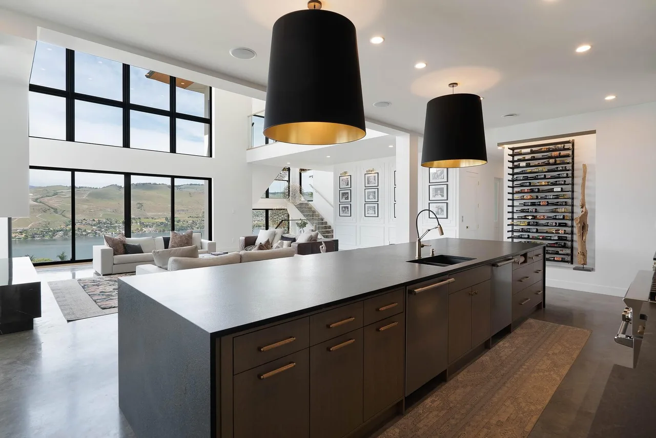 The kitchen island in dark wood and stone under black and gold pendants, looking toward the living room
