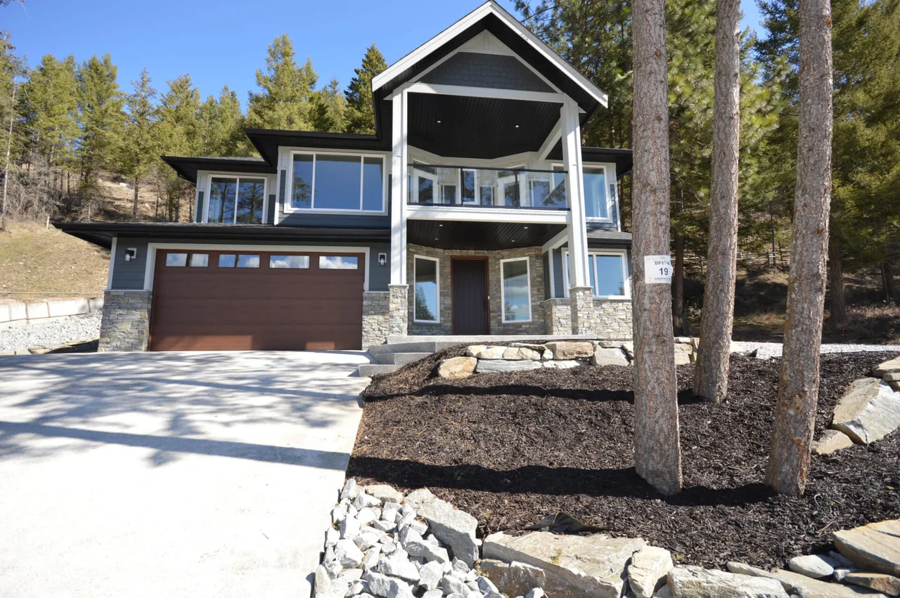 Millwood Garmisch from the street: a covered entry and balcony over a double garage among tall pines