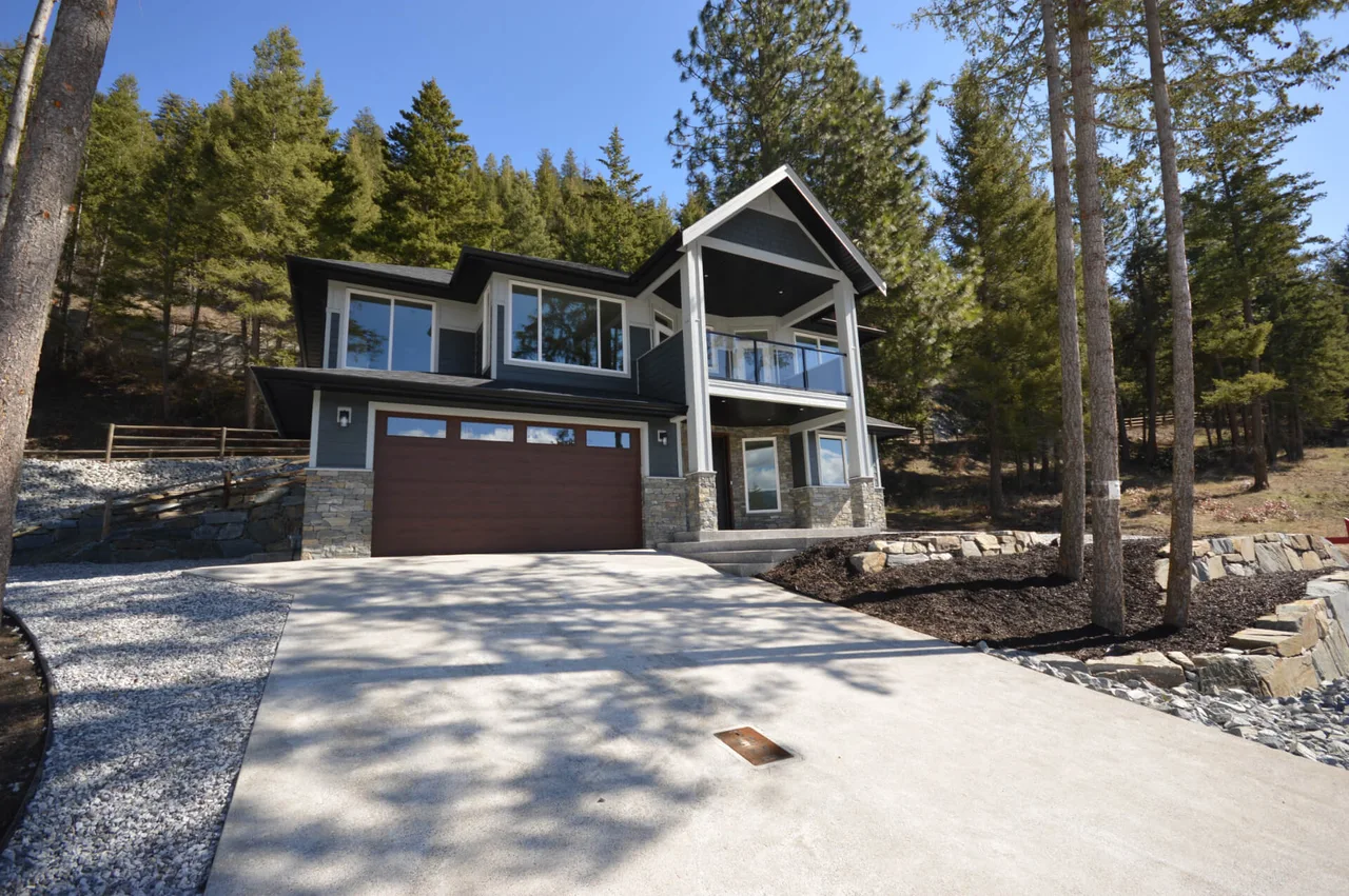 The front of the home behind a wide concrete driveway and natural stone landscaping