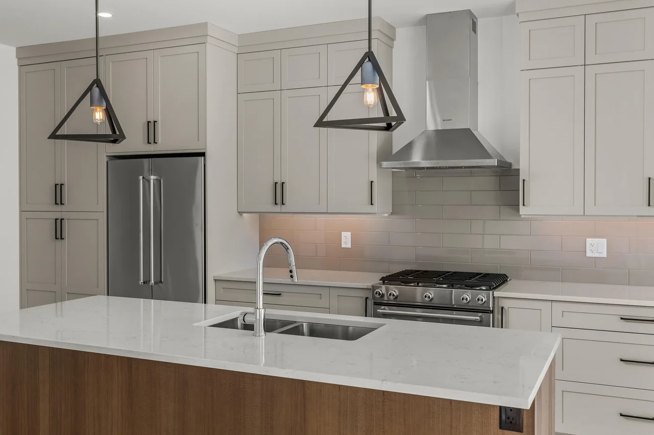 The kitchen sink in a white quartz island, with shaker cabinets and a stainless range