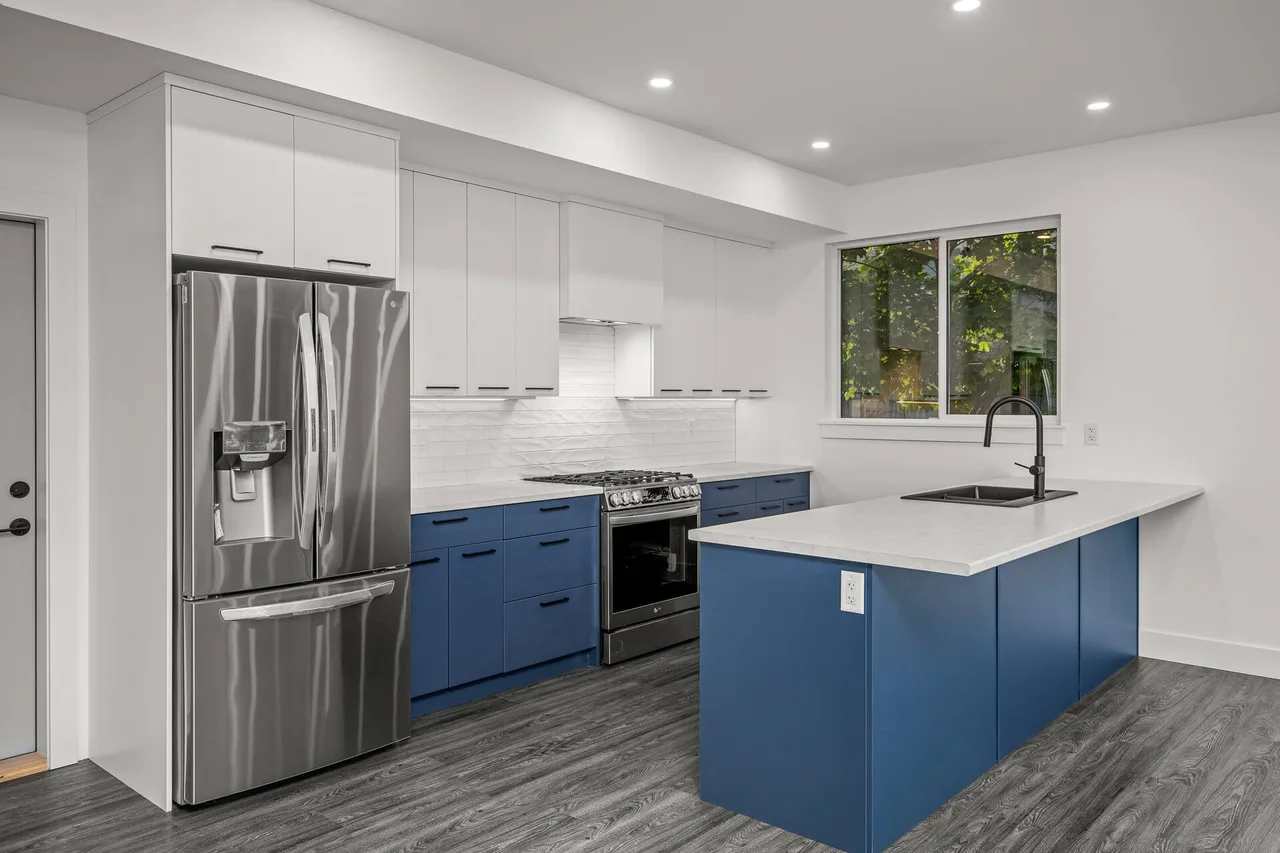The kitchen, with navy and white cabinets, a textured tile backsplash and stainless appliances