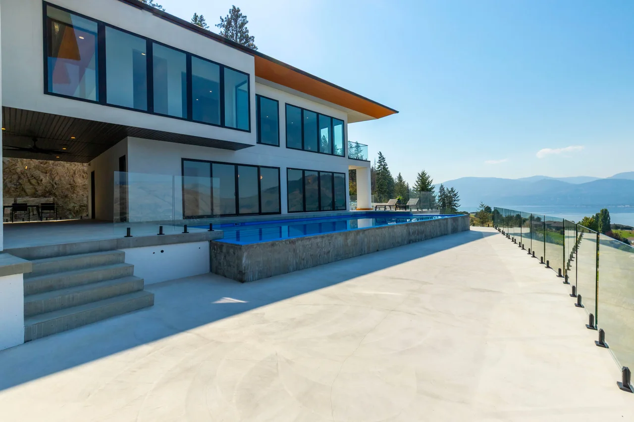 A modern hillside home with walls of glass, a pool deck and an infinity pool overlooking Okanagan Lake