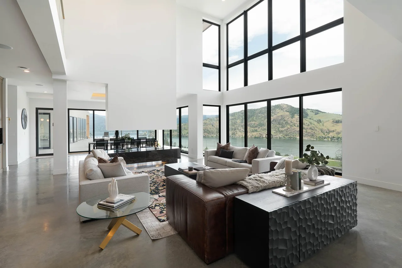 A double-height living room with floor-to-ceiling windows framing the lake and hills